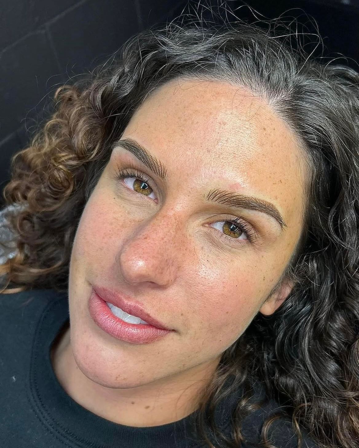Brow shaping close-up — curly-haired client with refined brow detail at Victoria Beauty atelier.