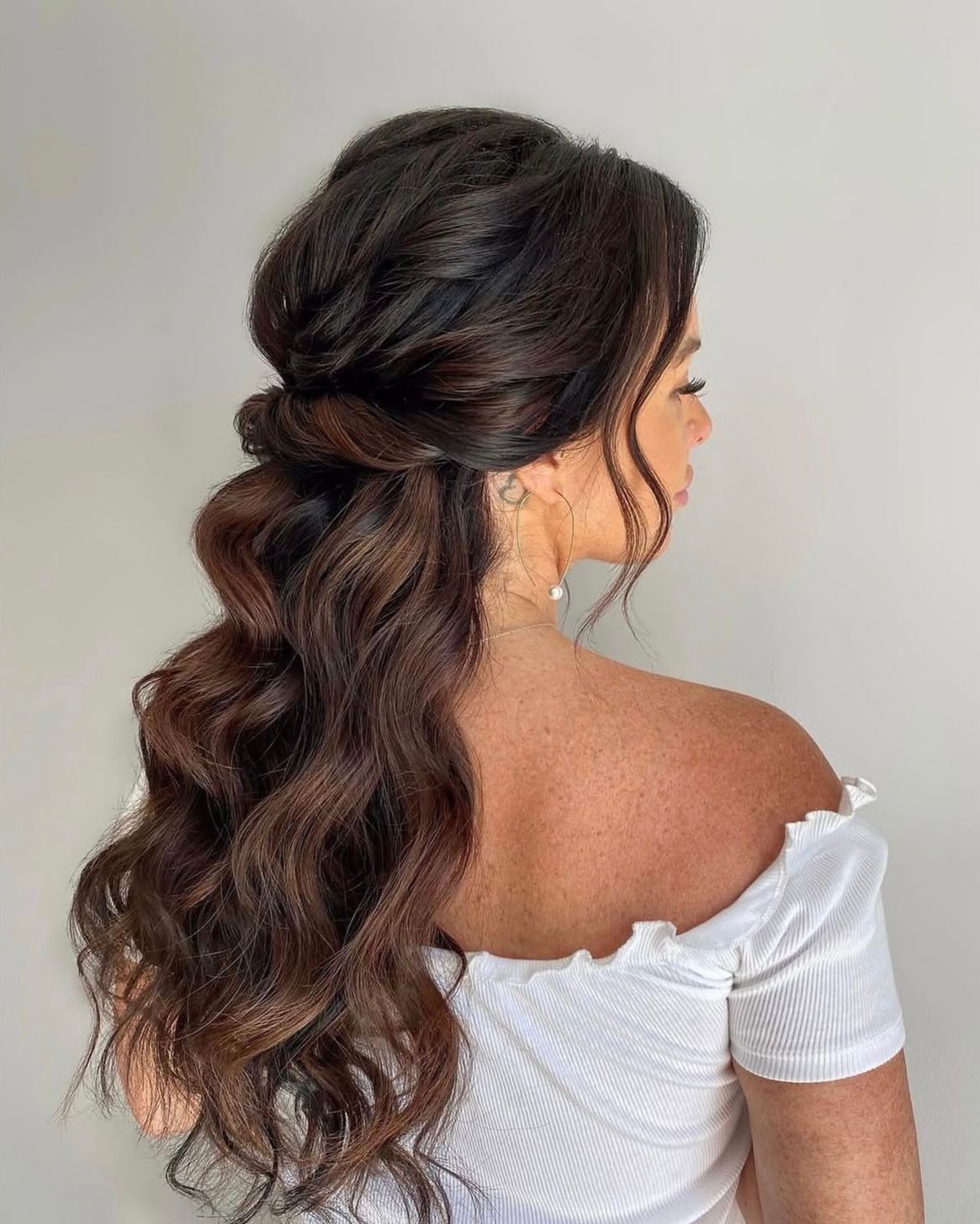 Editorial half-up styling with soft waves cascading over the shoulder.